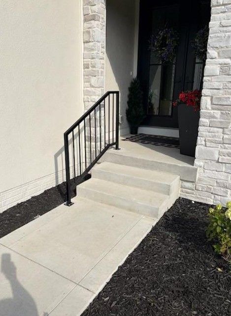 Front entrance with concrete steps, black handrail, and a dark doorway bordered by brick and white walls