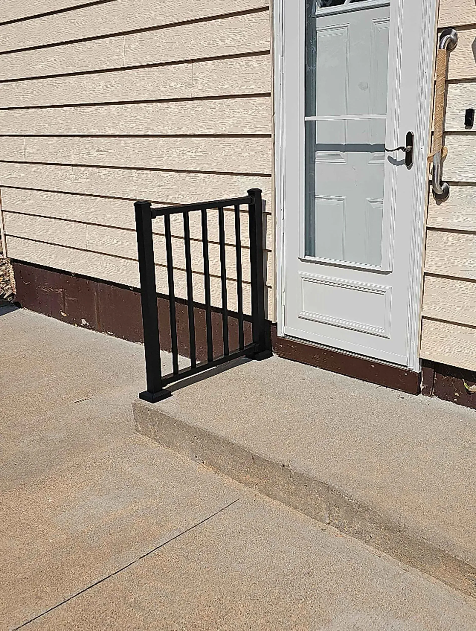 Black metal handrail next to a white door on a concrete step.