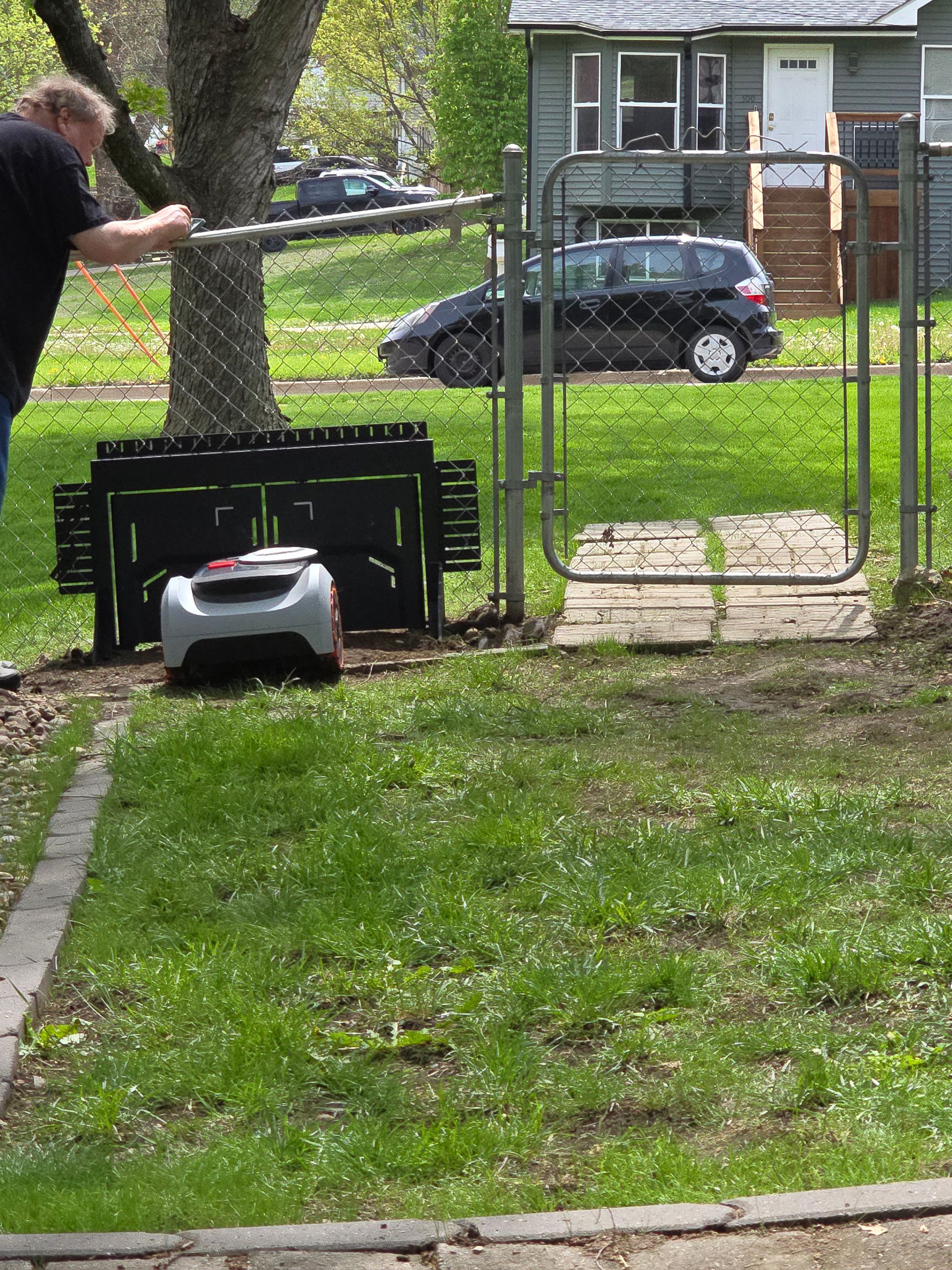 Person using a string trimmer beside a fenced yard with a small lawn mower on the grass