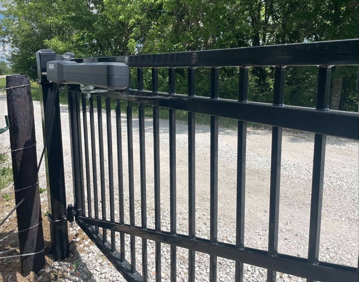 Black metal automatic gate with a motorized opener beside a gravel driveway in daylight
