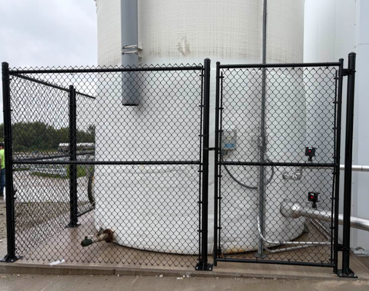 Chain-link fence enclosing large white industrial tanks with pipes and valves.