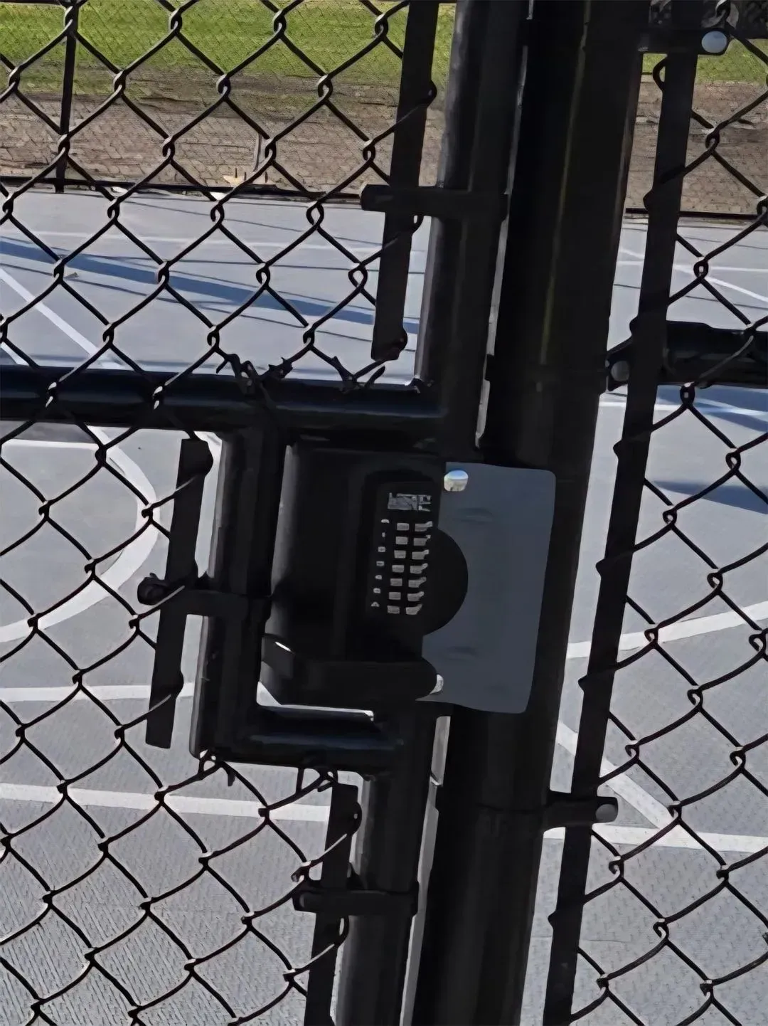 Black gate with keypad lock on chain link fence, likely securing an outdoor area.