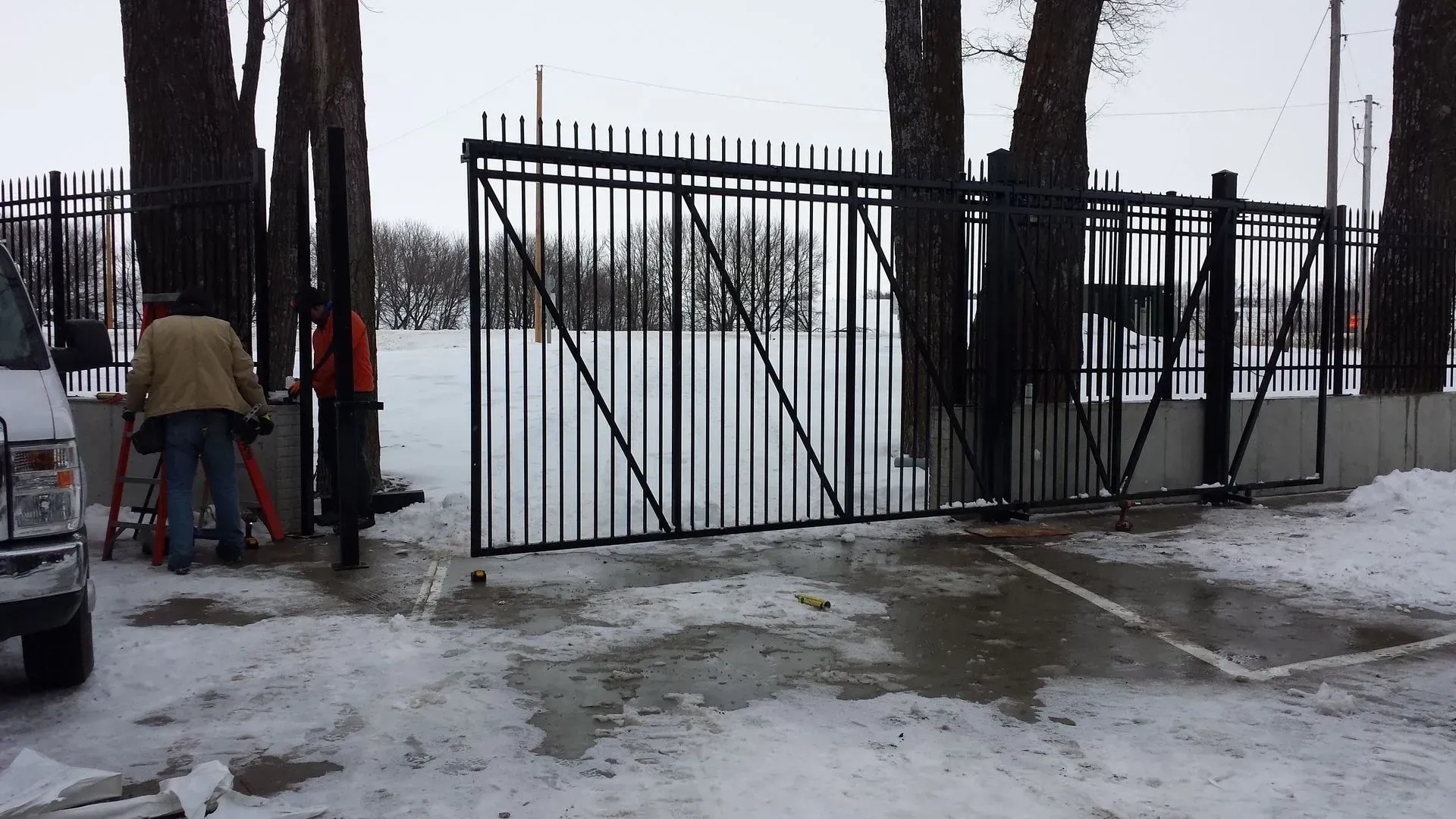 Black metal gate, partly open, in snowy area. Person working on the left.