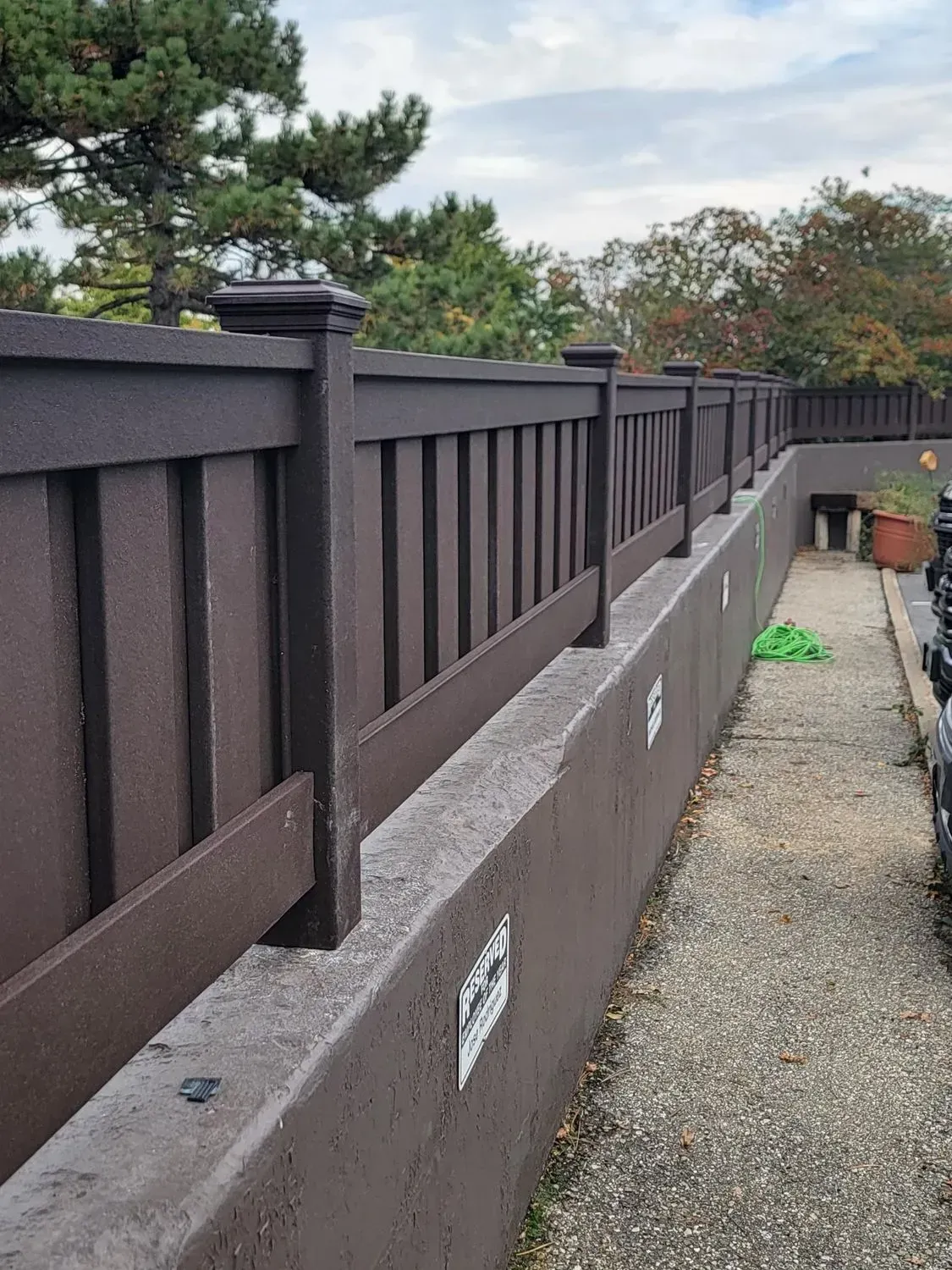 Brown fence on a concrete barrier along a narrow walkway.