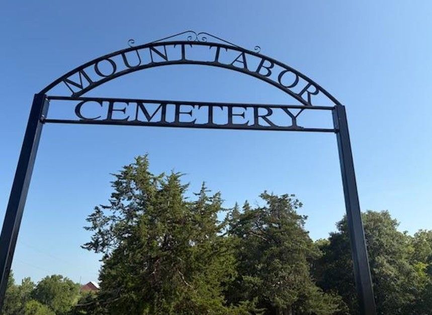 Mound Bayou Cemetery arch sign against a blue sky, framed by trees
