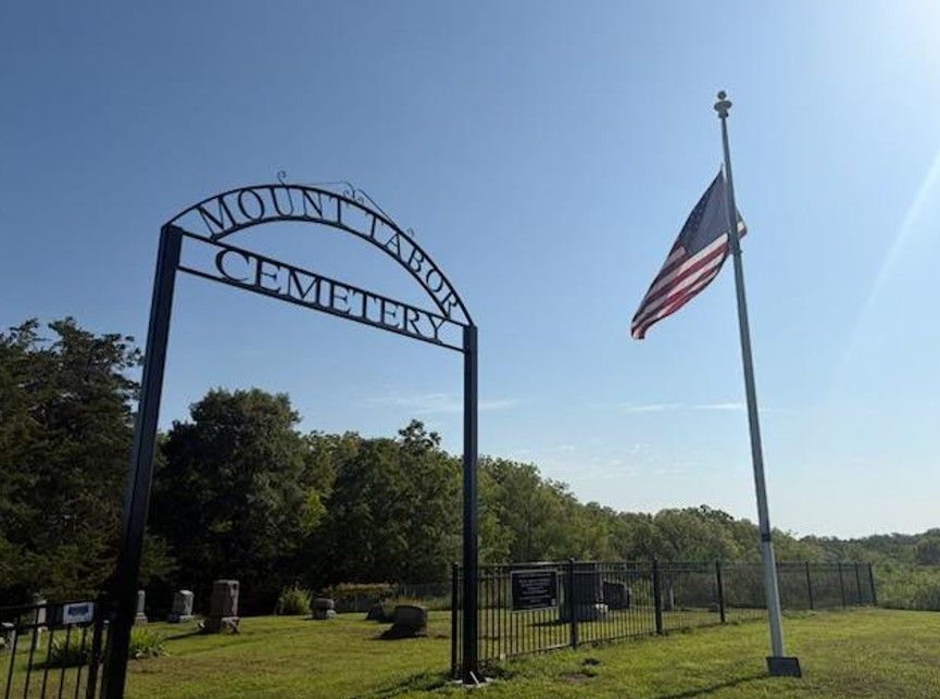Entrance sign to Mount Moriah Cemetery beside a U.S. flag on a grassy field