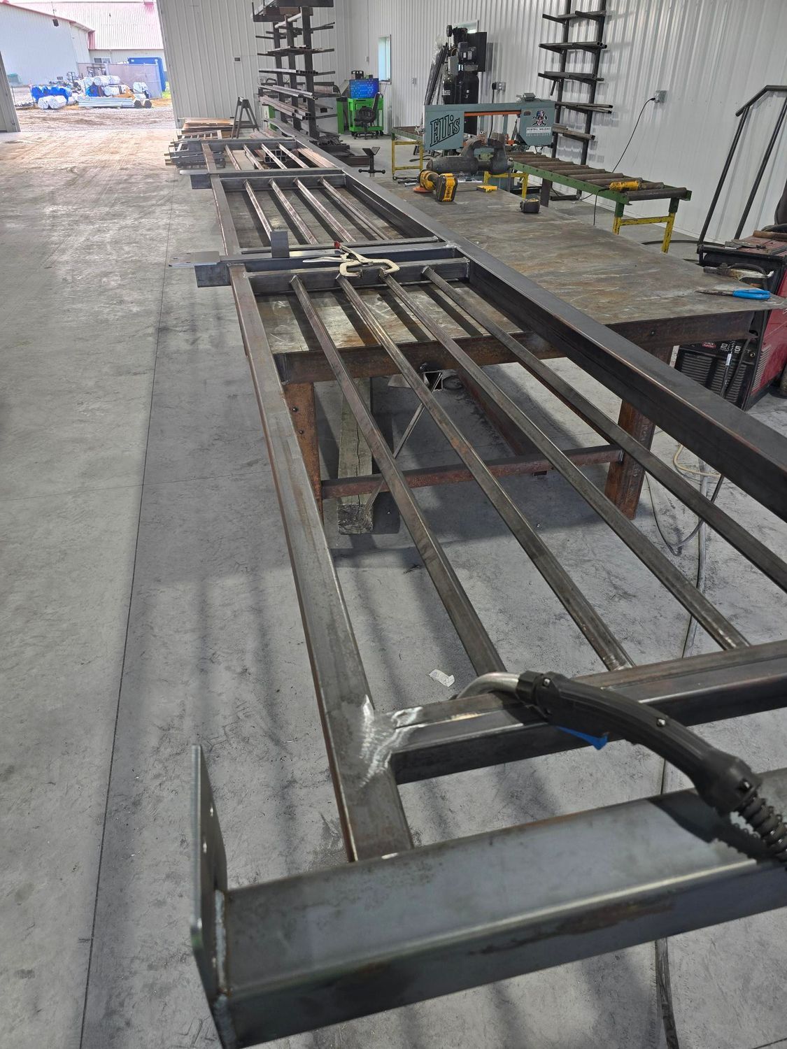 Rows of metal beams laid on a workshop floor beside a workbench and tools