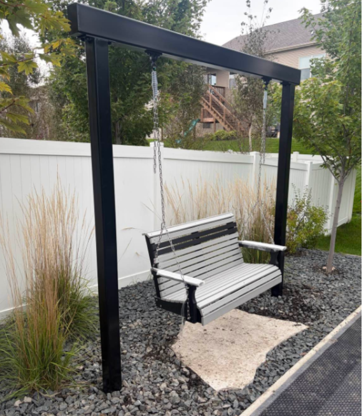 Black metal swing bench over gravel in a fenced backyard garden