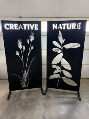 Two black standing metal panels featuring cut-outs of wheat and a leaf stem, with the words 