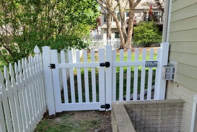 White picket fence with a double gate leading to a backyard.
