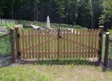 Wooden gate in a grassy yard, leading to a garden area with trees and a white umbrella.
