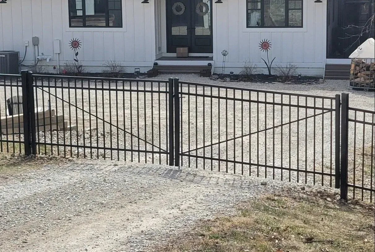 Black metal fence and gate in front of a white house with gravel driveway.