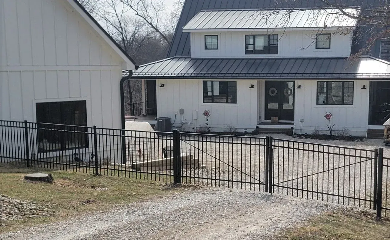 White house with black metal fence and gravel driveway.