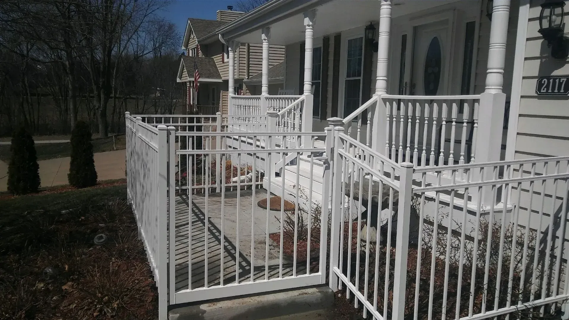 White metal fence and gate surrounding a front porch of a house with steps.