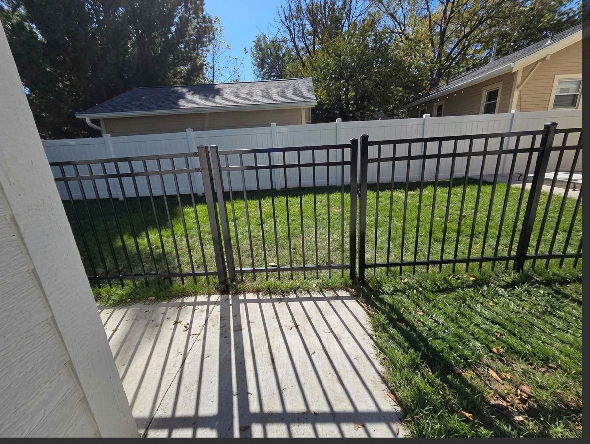 Black metal fence and gate casting shadows across a concrete patio in a sunny backyard