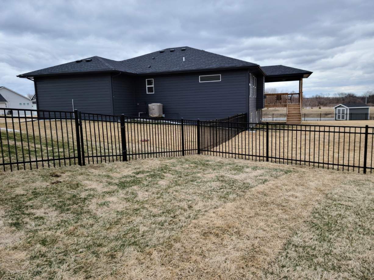 Dark blue house with a black metal fence and a covered patio on a cloudy day.