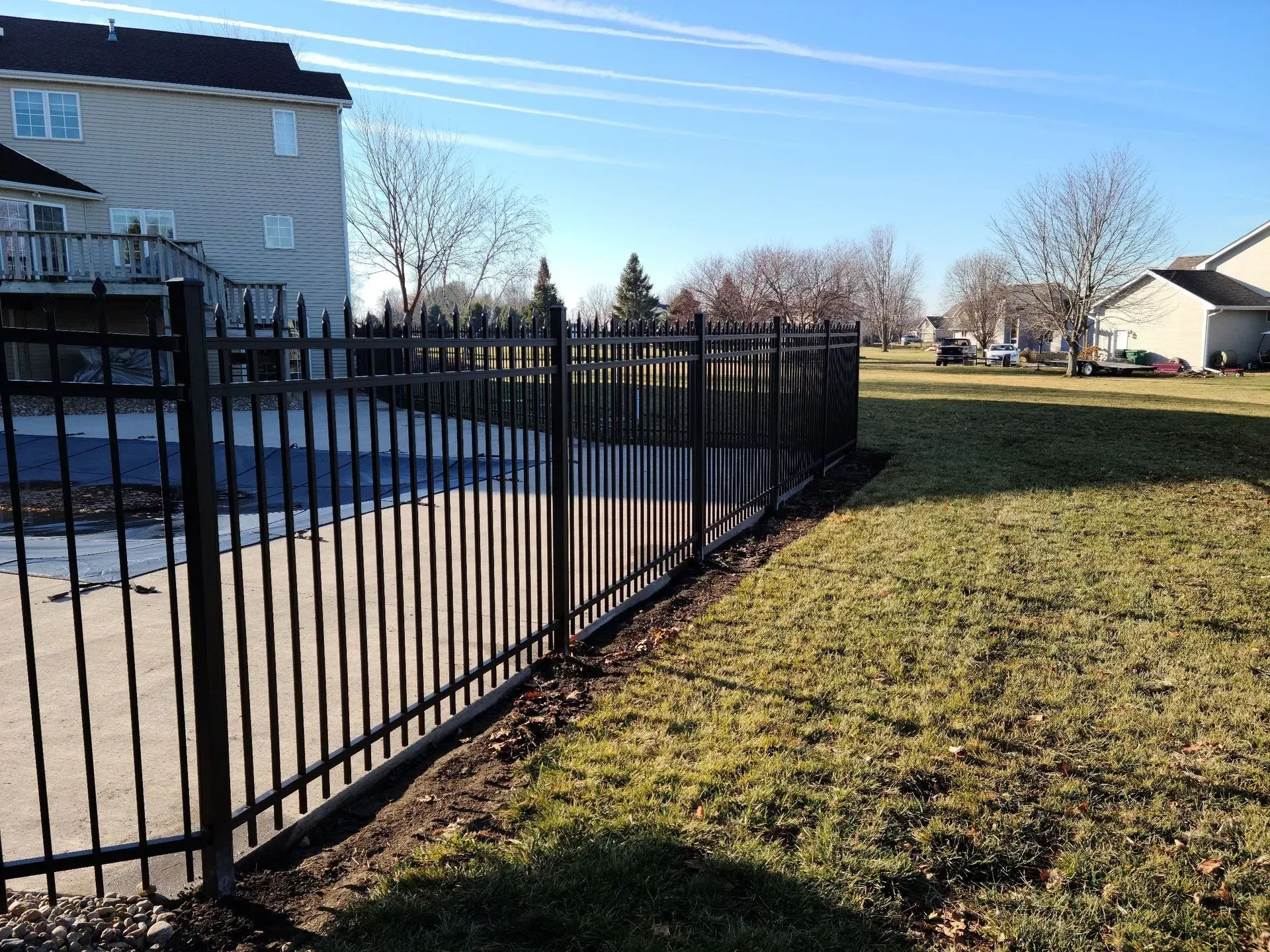 Black metal fence bordering a driveway and grassy yard on a sunny day.