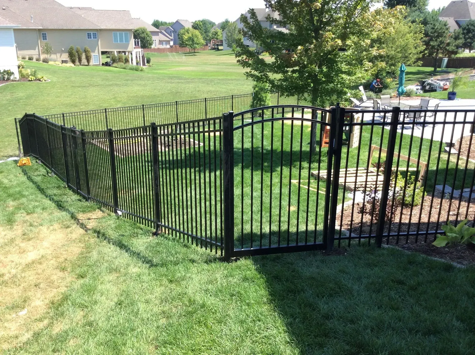 Black metal fence with gate in a grassy backyard.
