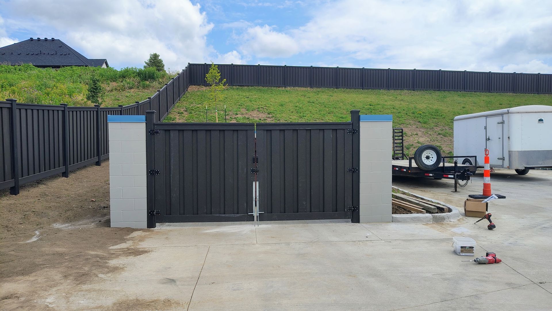 Driveway gate with black metal panels and concrete pillars in a landscaped yard.