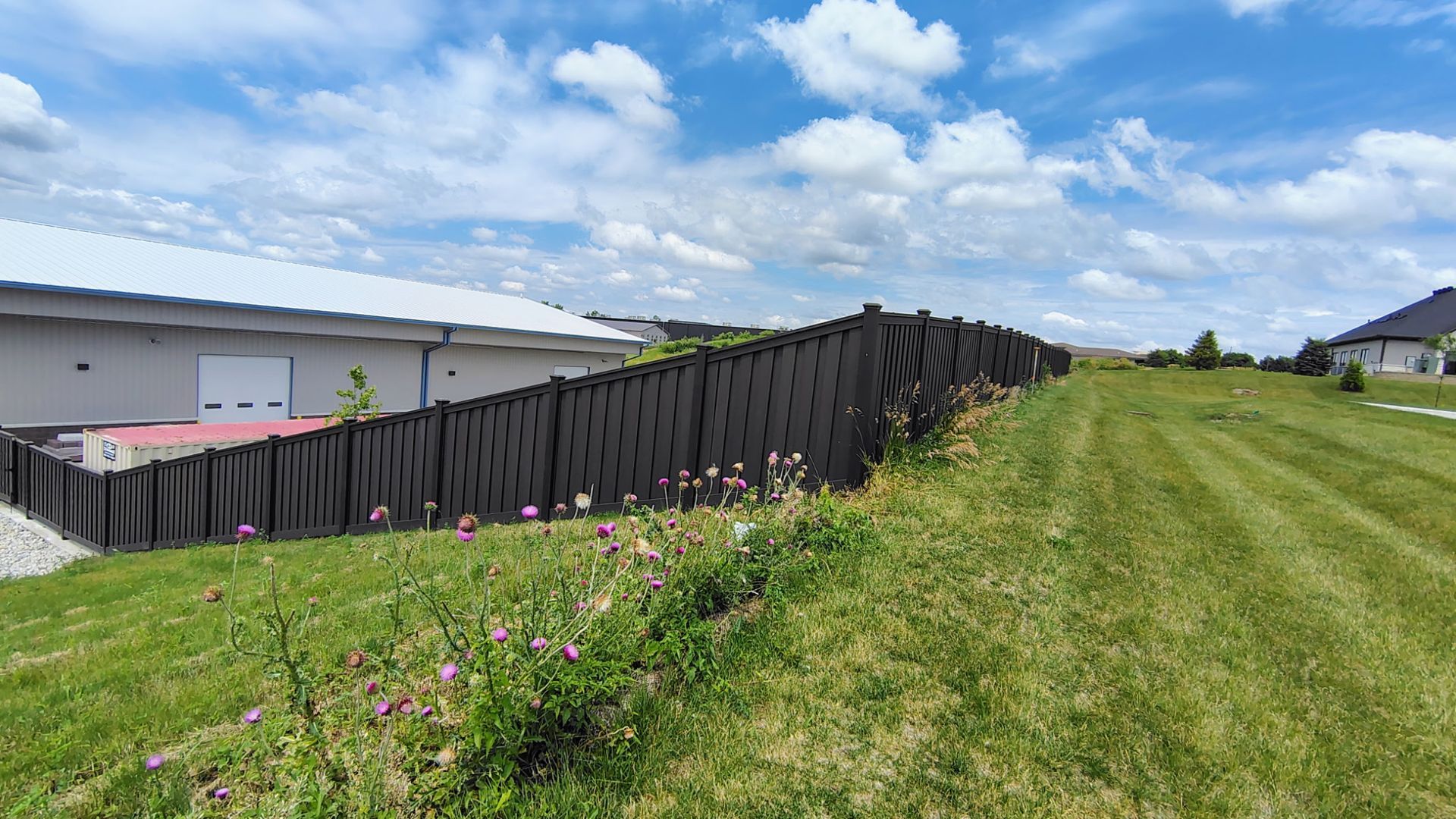 Wooden fence beside a grassy path under a bright blue sky with scattered clouds