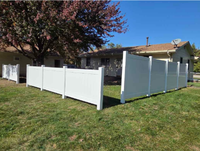 White vinyl privacy fence around a grassy yard beside a house under a blue sky
