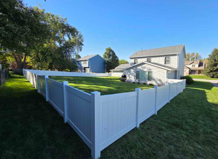 White Vinyl fenced backyard with green lawn and a two-story house on a sunny day