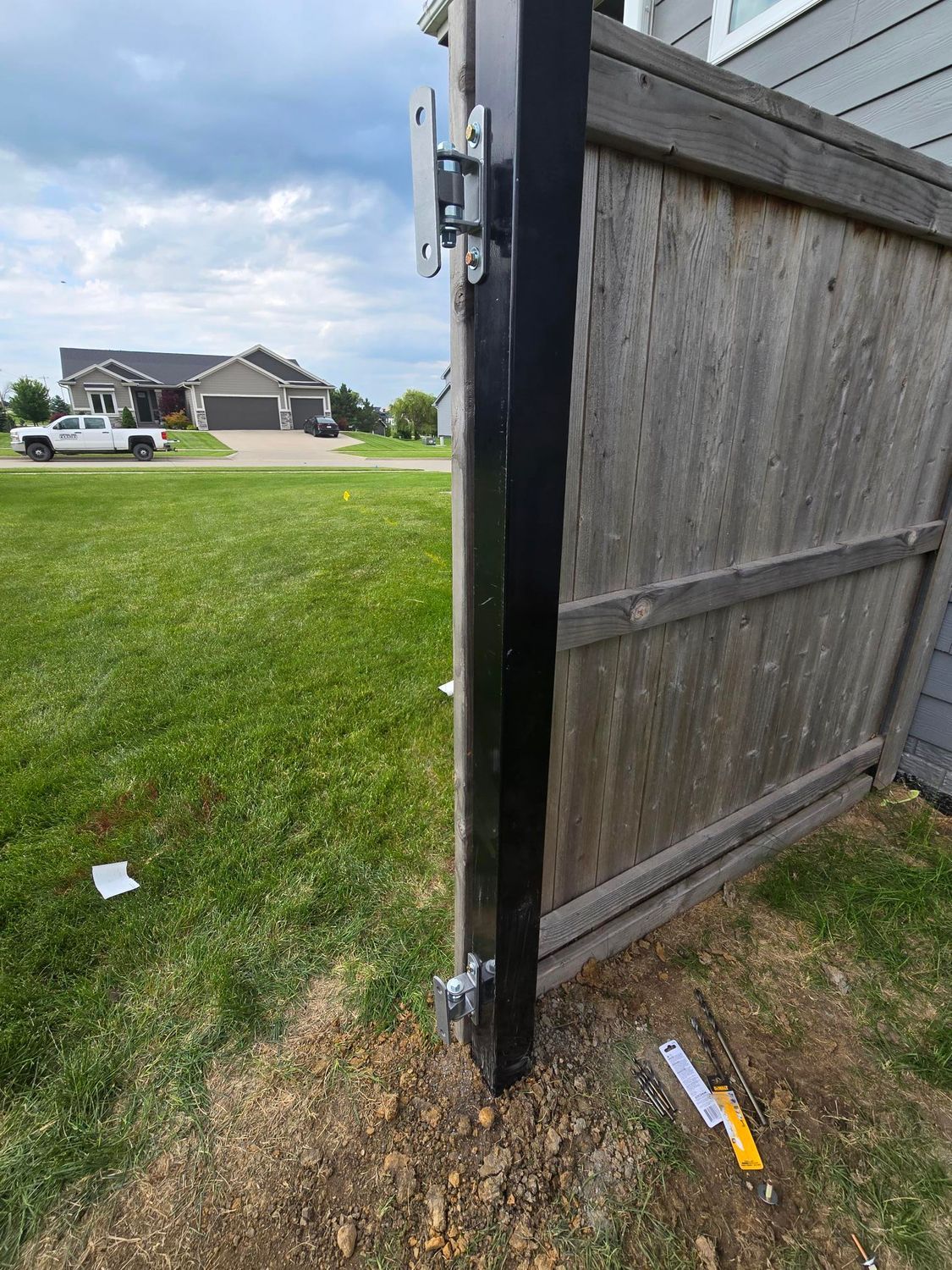 Open wooden gate with metal latch, beside a grassy suburban yard and street.
