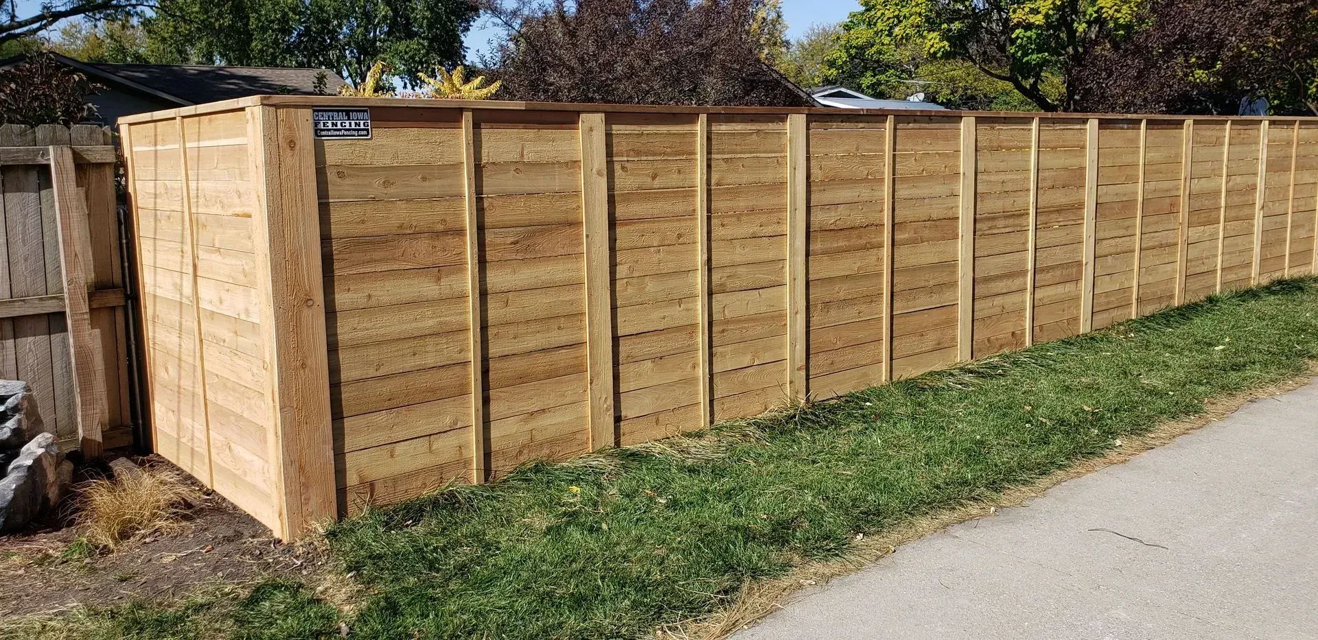 Wooden fence next to grass and a sidewalk.
