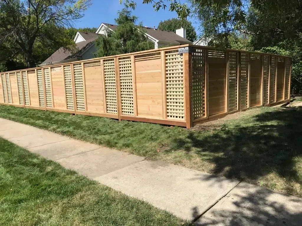 Wooden fence with lattice panels along a sidewalk, grass, and trees.