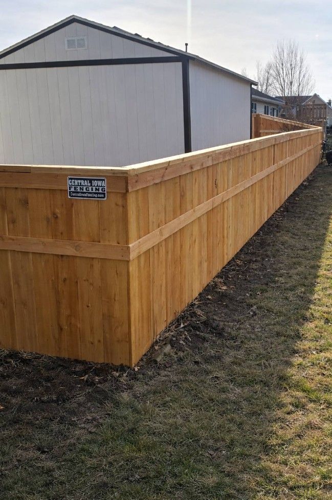 A long, newly installed wooden privacy fence runs alongside a white shed