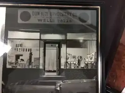 A black and white photo of a store front with a car parked in front of it.