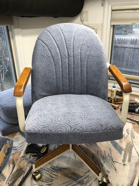 A blue chair with wooden arm rests is sitting on a rug in front of a window.