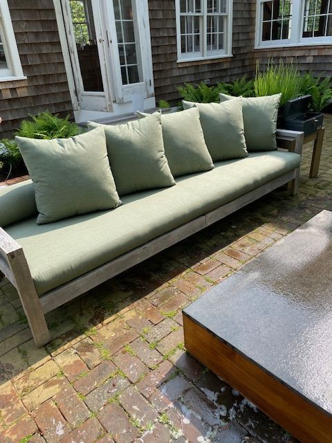 A couch with green pillows sits on a brick patio
