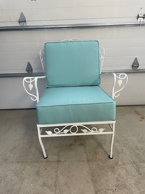 A white chair with a blue cushion is sitting in front of a garage door.