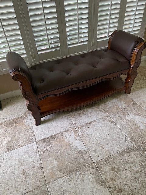 A brown bench is sitting on a tiled floor next to a window.