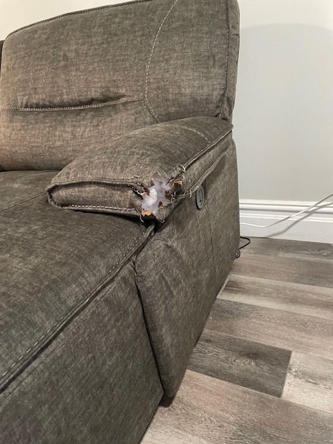 A couch with a broken arm rest is sitting on a wooden floor.