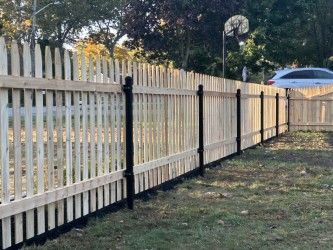 A white picket fence with black posts is sitting in the middle of a grassy field.