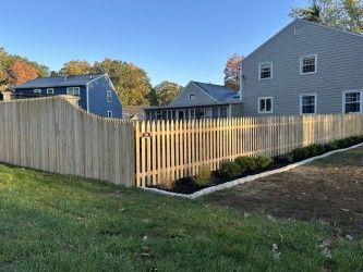 A wooden fence surrounds a lush green yard in front of a house.