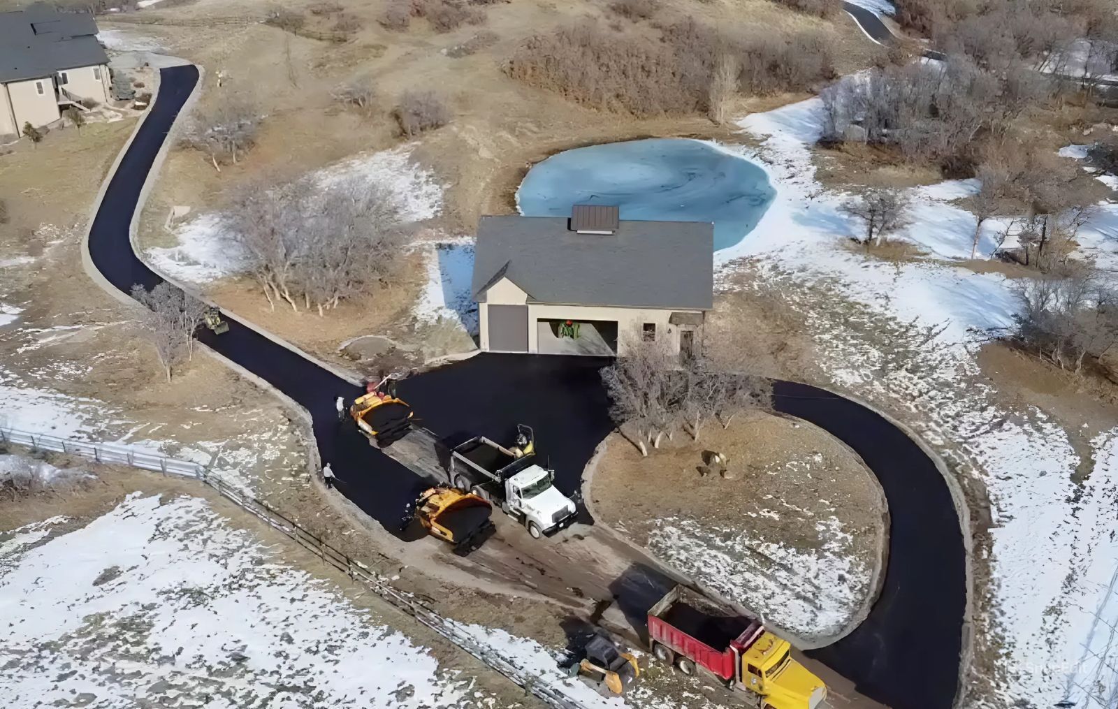 An aerial view of a road being paved in front of a house.