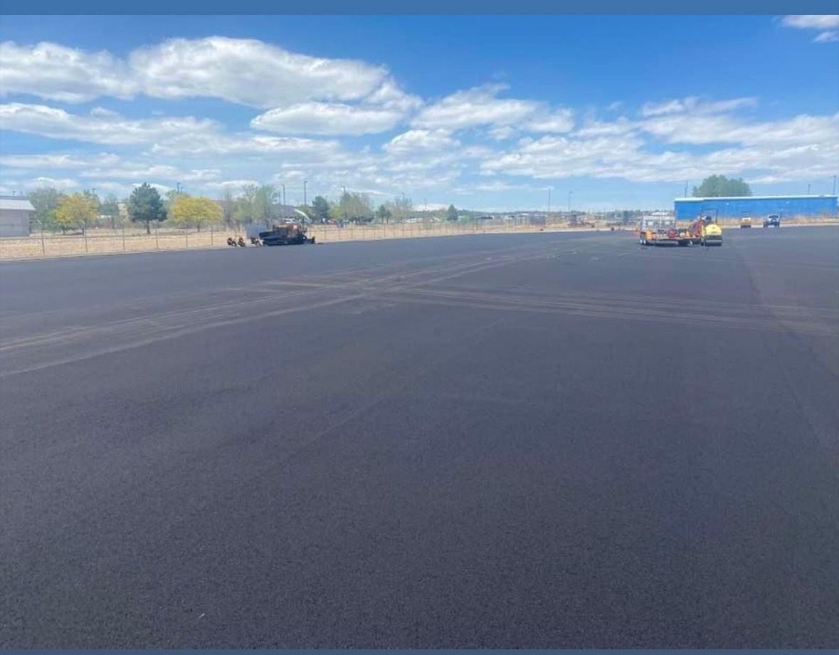 A large empty parking lot with a blue sky and clouds in the background.