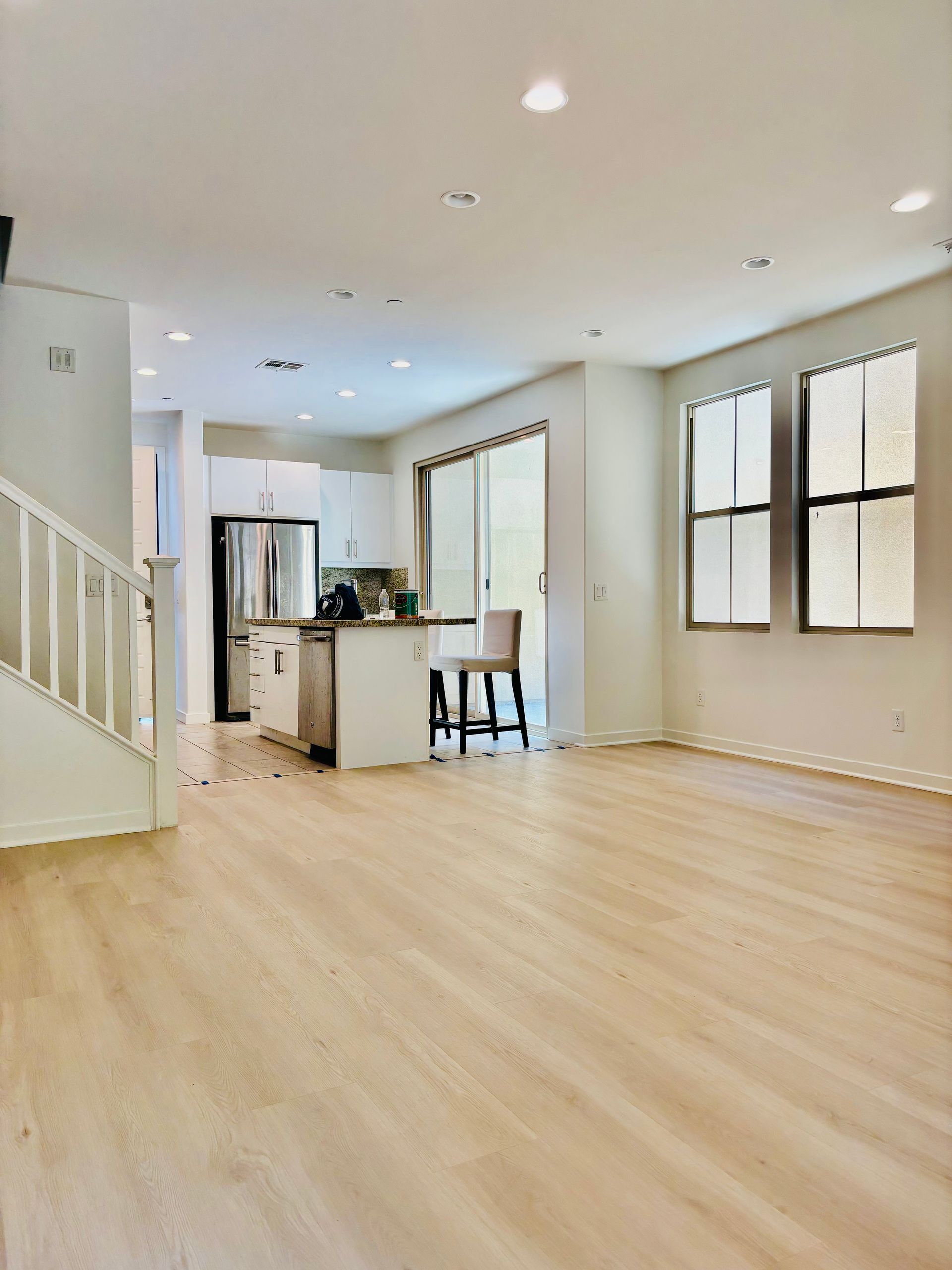 An empty living room with hardwood floors and a kitchen in the background.