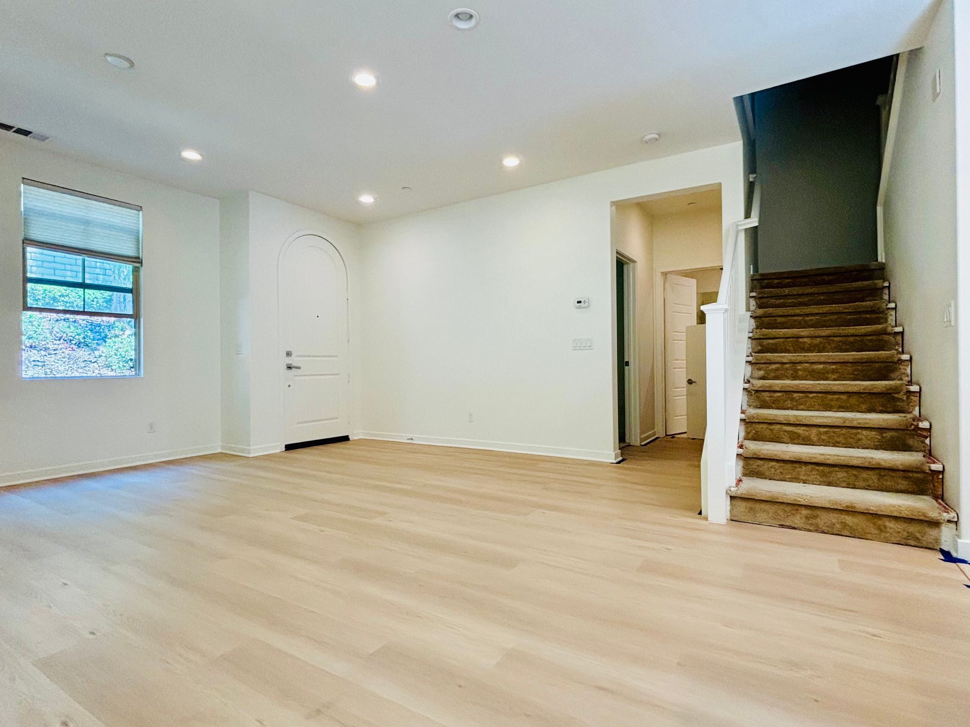 An empty living room with hardwood floors and stairs leading up to the second floor.