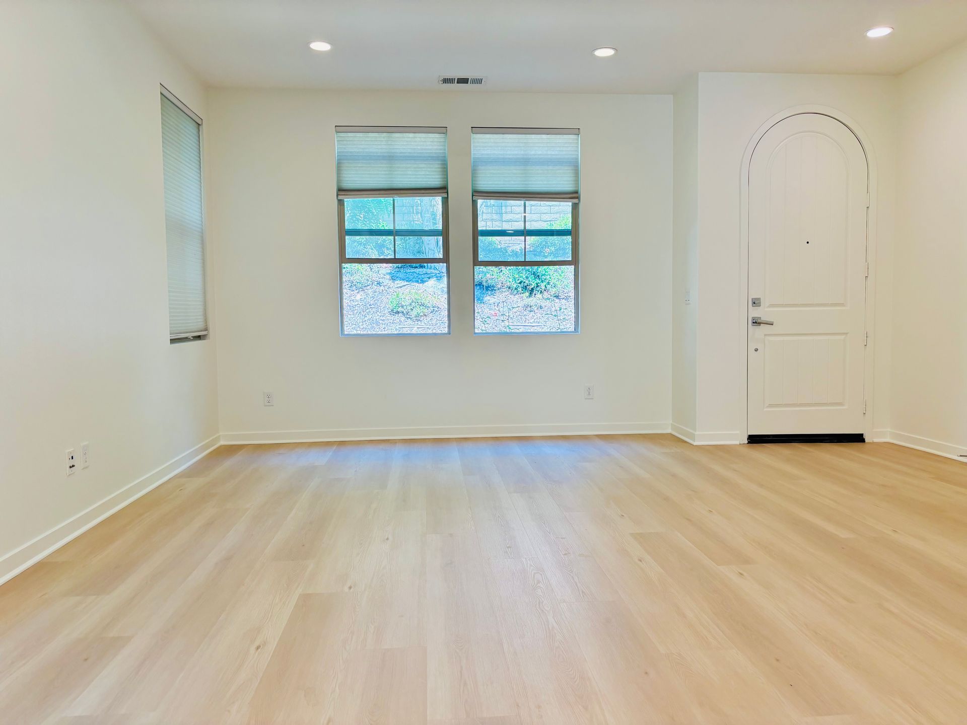 An empty living room with hardwood floors and two windows.