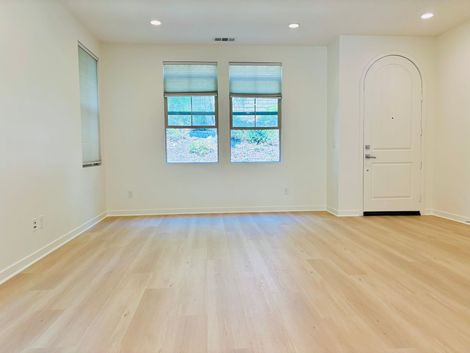 An empty living room with hardwood floors and two windows.