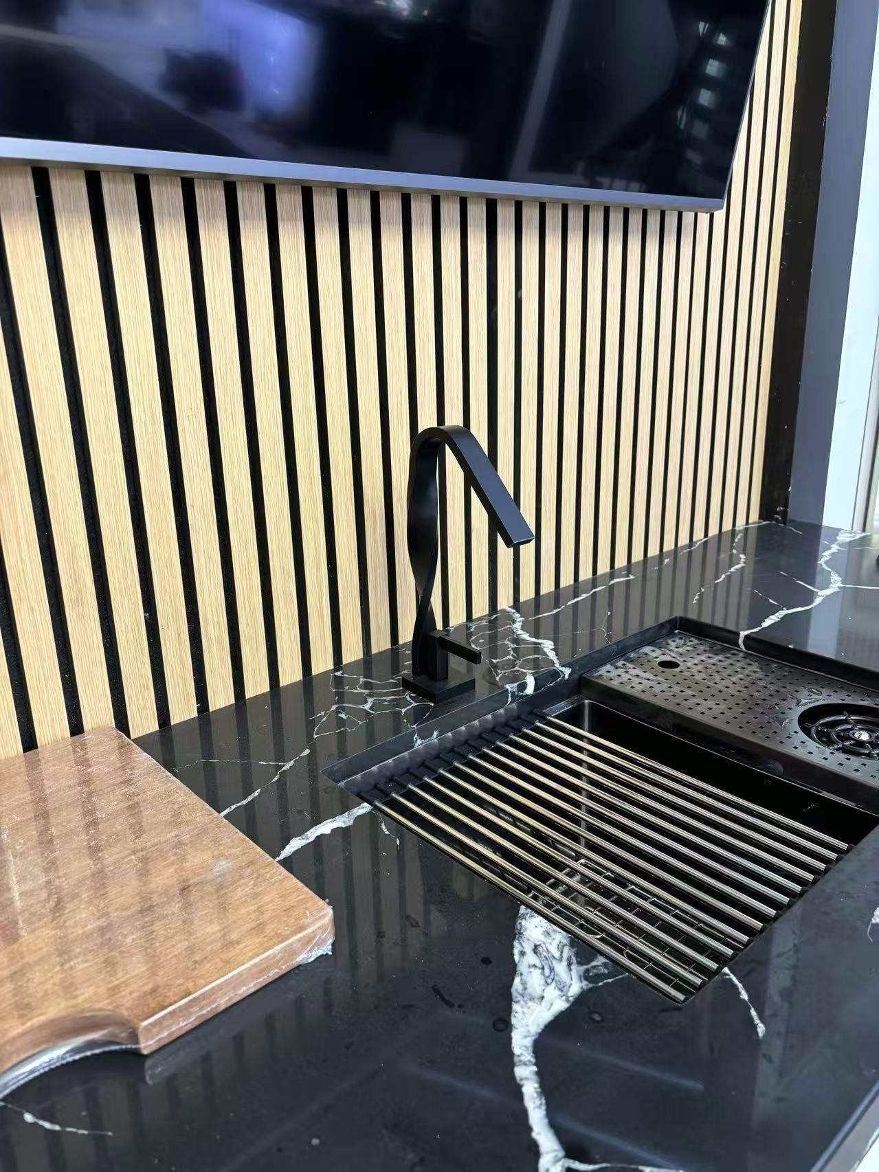 A kitchen counter with a sink , cutting board , and television.