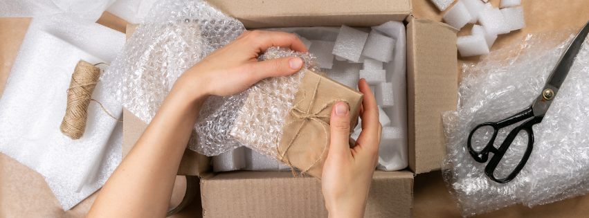 A person is packing a box with bubble wrap and scissors.