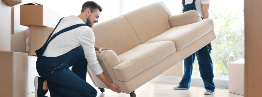 Two men are moving a couch in a living room.