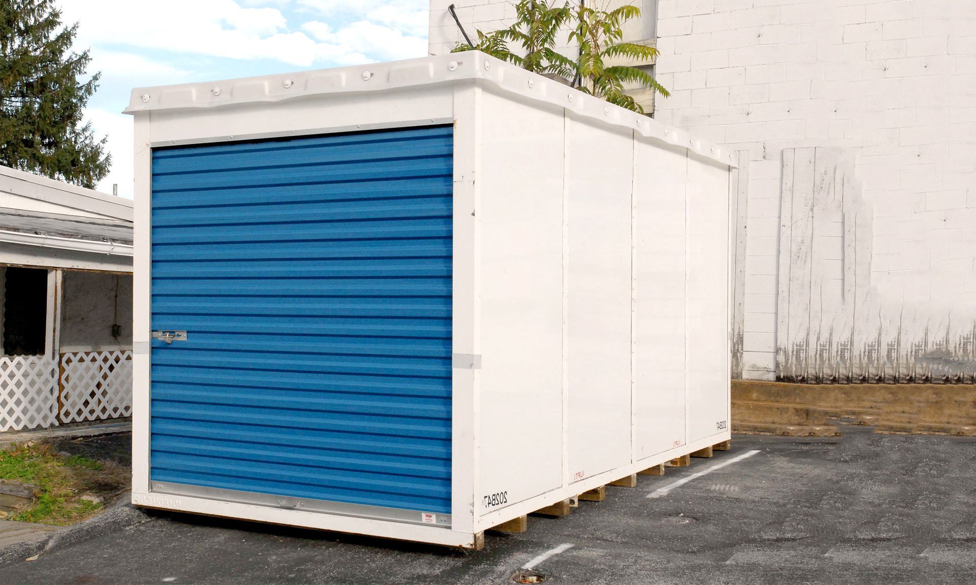 A white shed with a blue door is sitting in a parking lot.