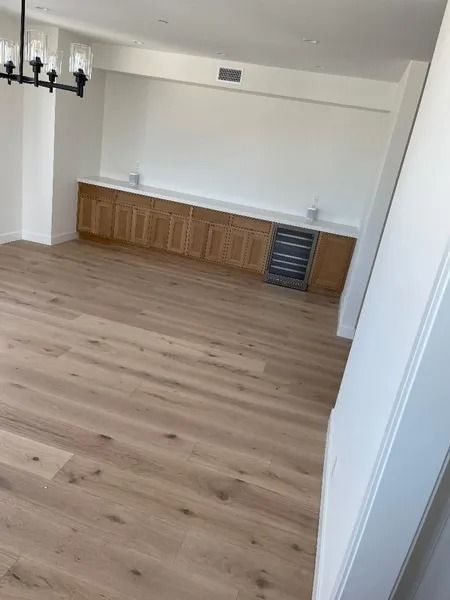 Empty room with light wood floors, a built-in wooden cabinet with a wine fridge, and white walls.