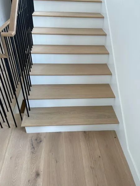 Wooden staircase with white risers and black metal railing, leading upwards.